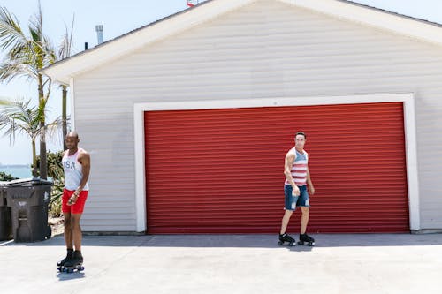 Two Men Roller Skating Near a Building with Red Roller Shutter