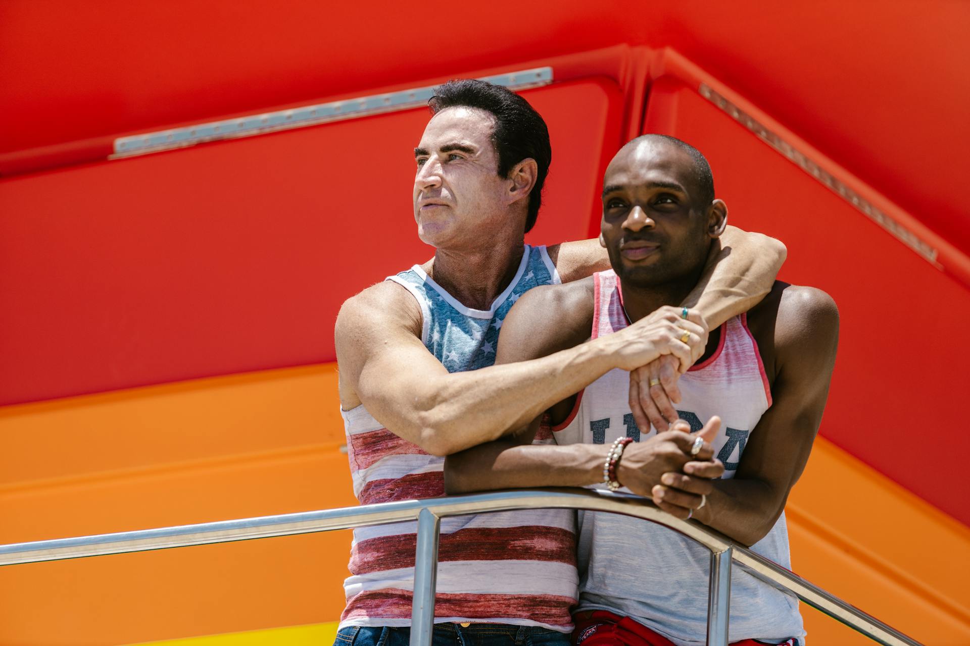 Interracial gay couple bonding outdoors with vibrant background.