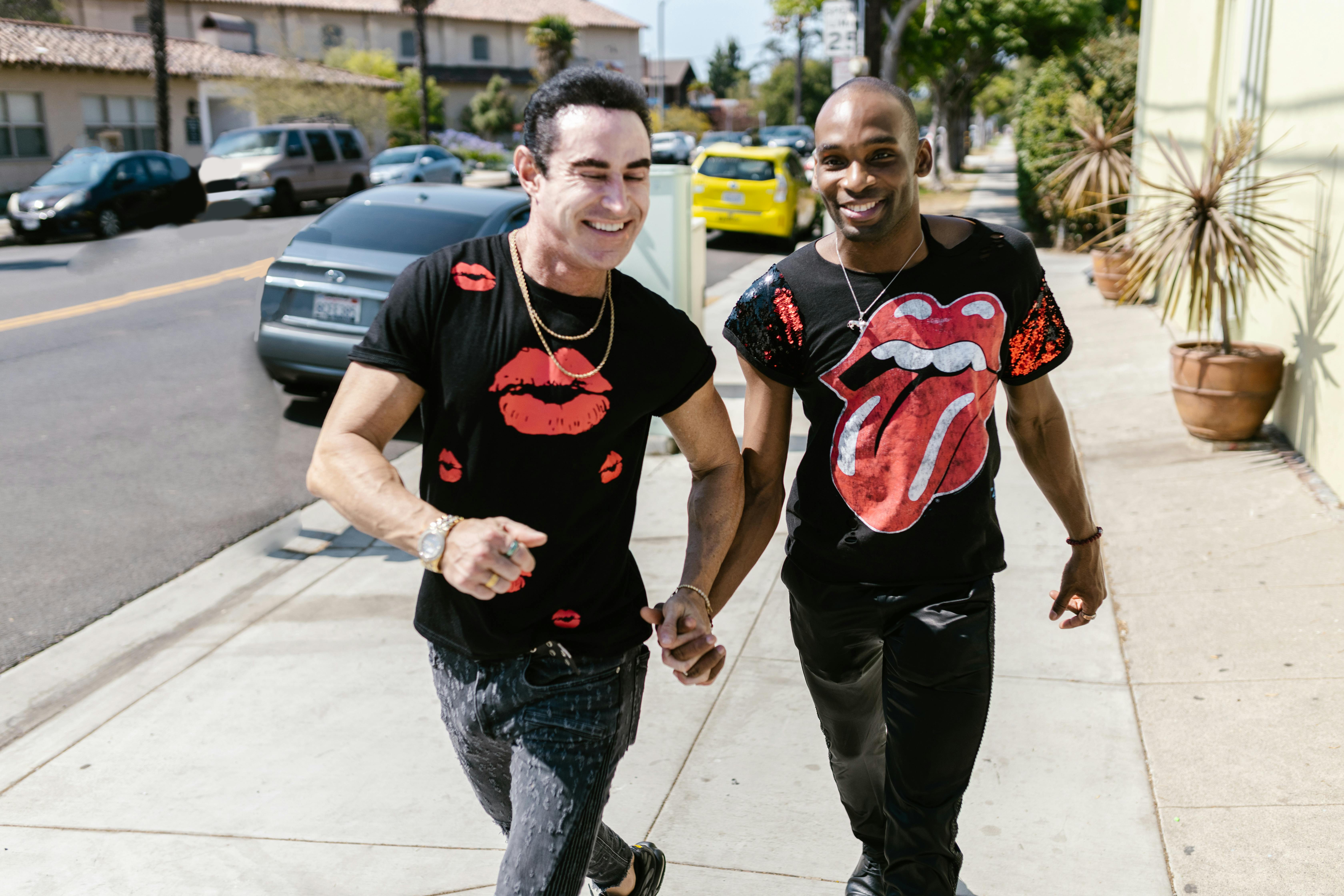 two men holding hands while walking on sidewalk