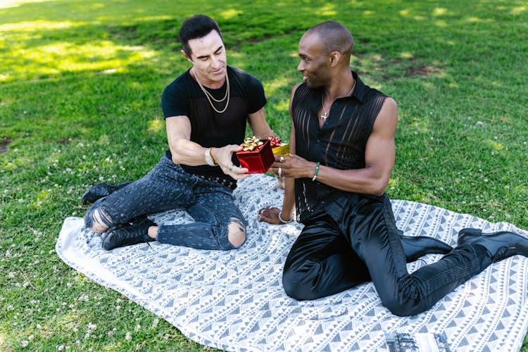 Couple Exchanging Gifts Sitting On Picnic Blanket