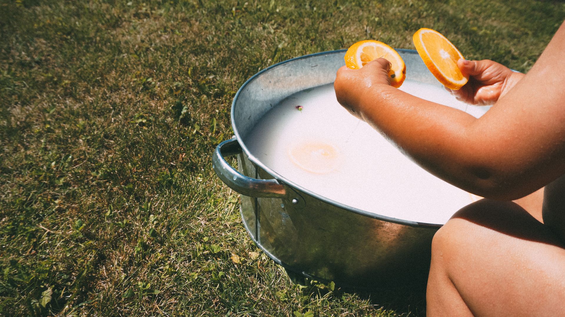A woman using orange slices in a milk bath outdoors for a natural skincare routine.