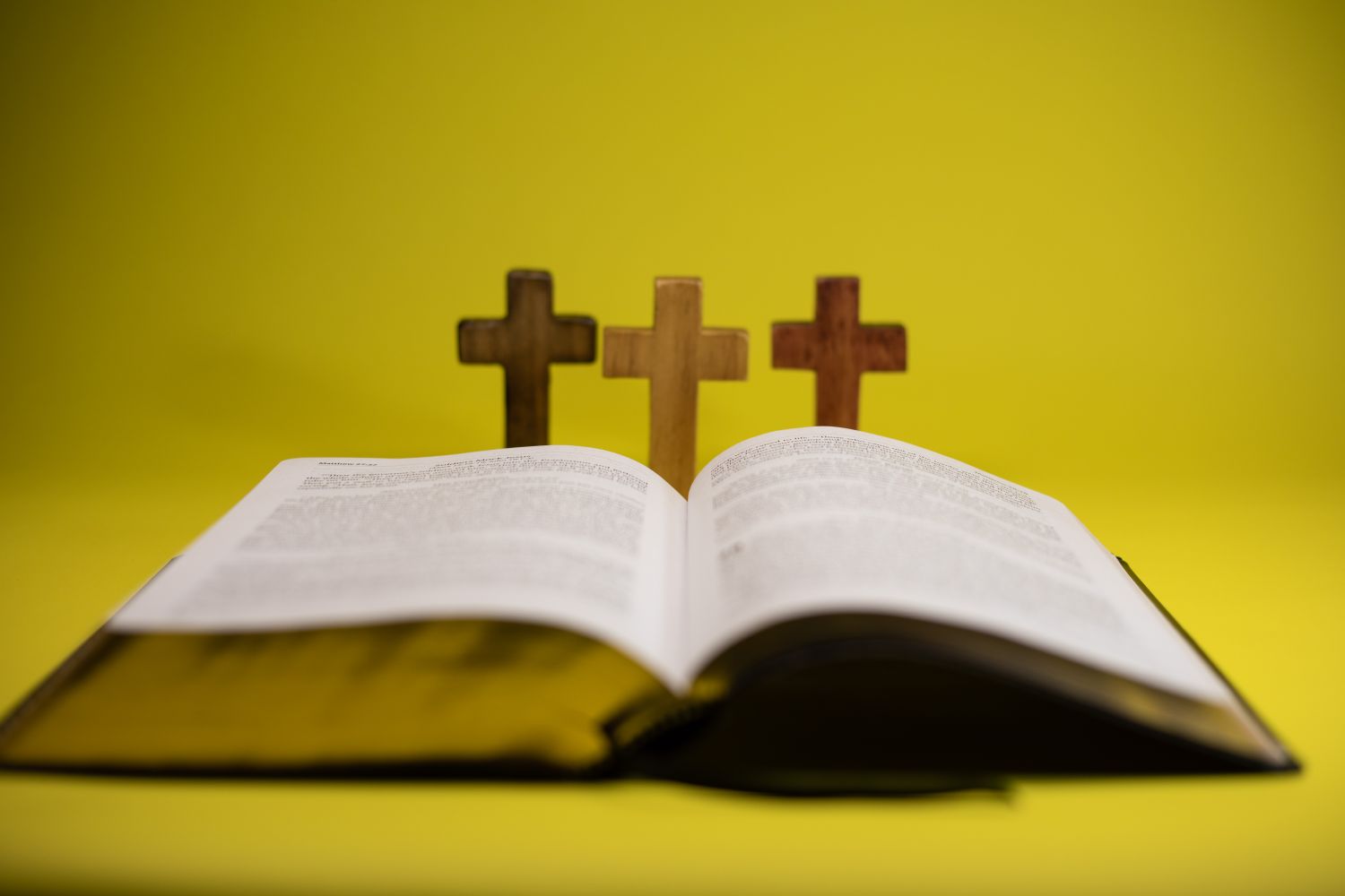 An open Bible with three crosses displayed against a vibrant yellow backdrop.