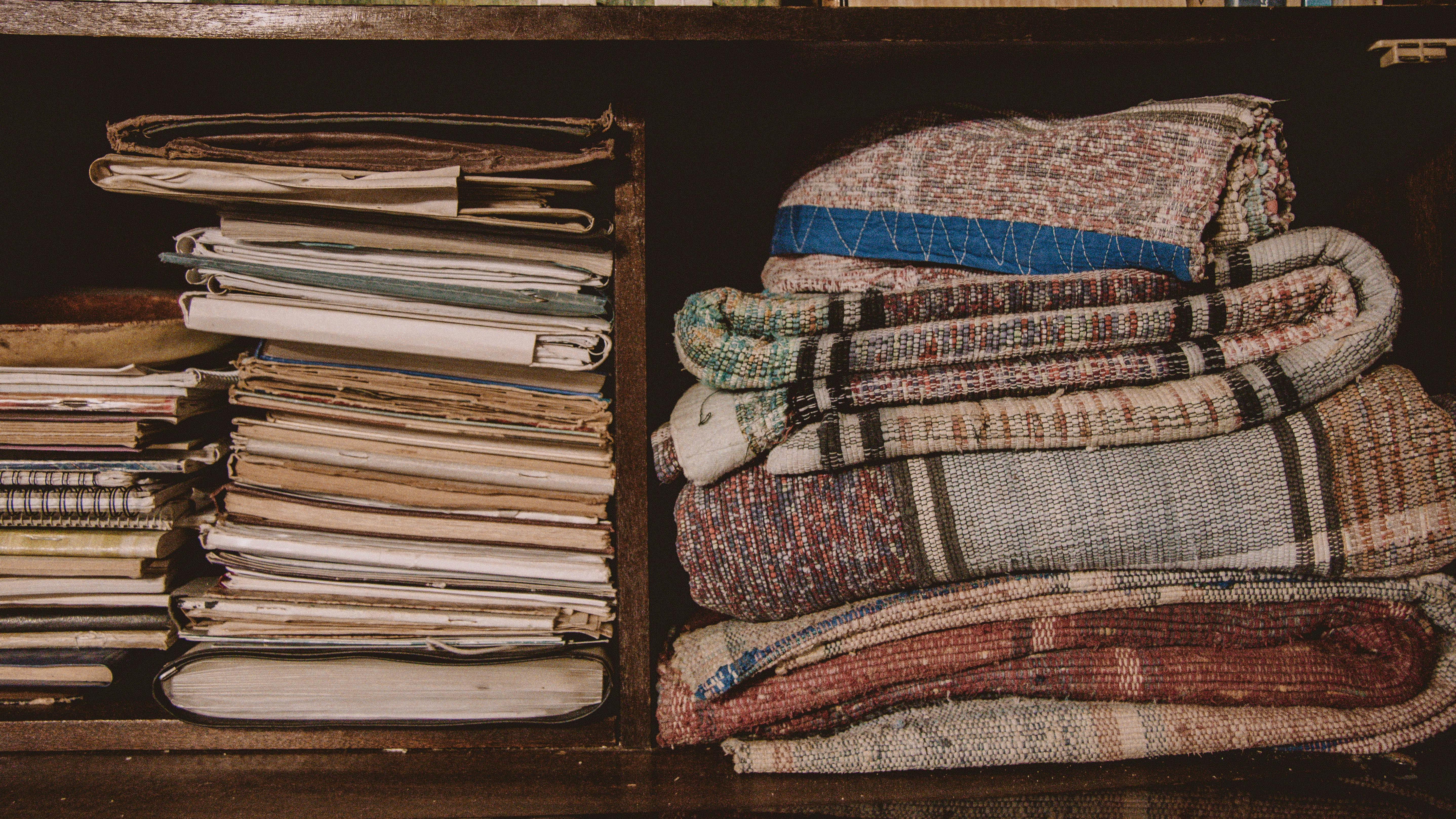 Close-up of stacked books and colorful textiles on a wooden shelf.