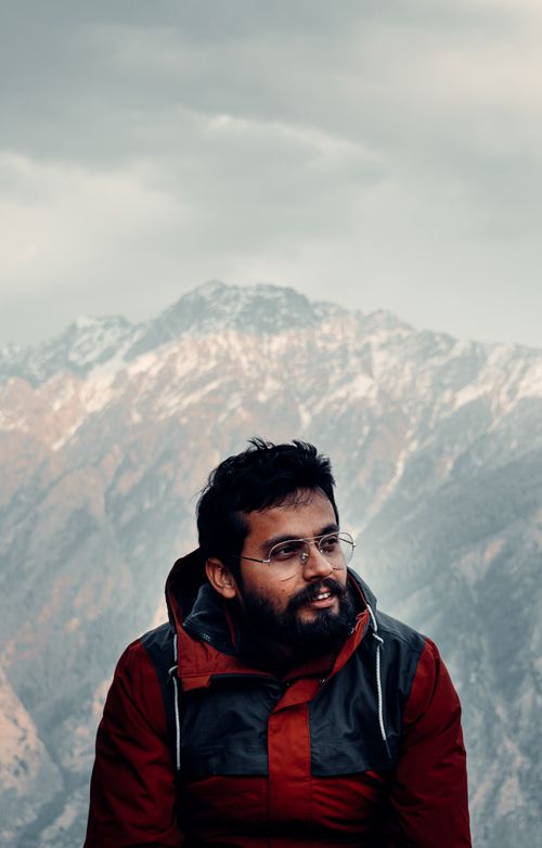 Free A bearded man with glasses smiles in front of snow-covered mountains, creating a serene outdoor portrait. Stock Photo
