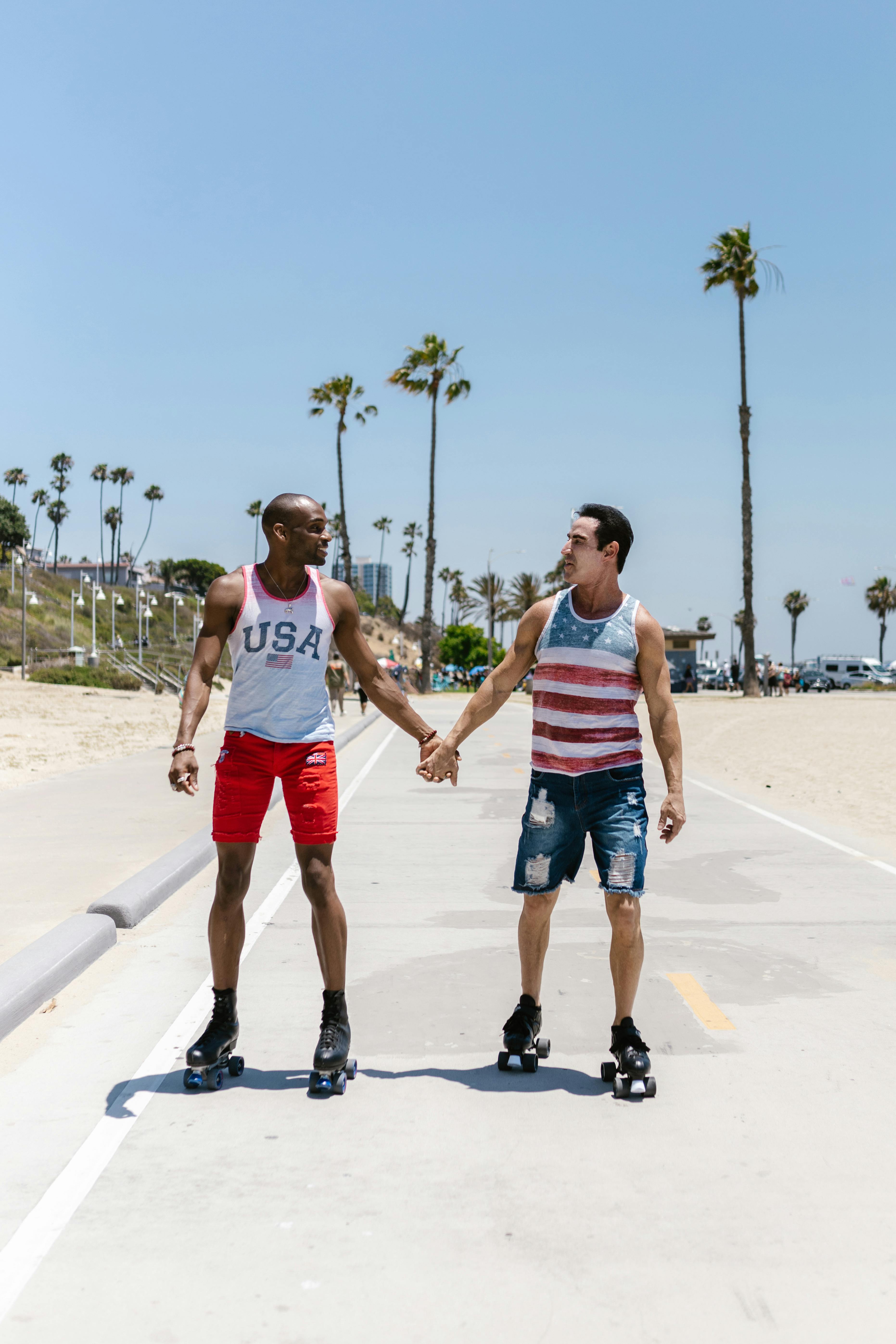 Couple enjoying roller skating by the beach, holding hands under the clear blue sky.