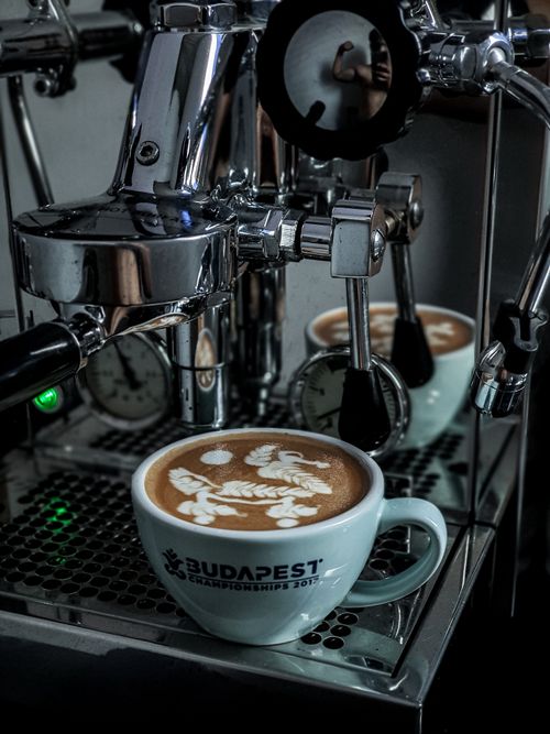 Free Close-up of latte art in a cup against a professional espresso machine. Perfect for coffee enthusiasts. Stock Photo