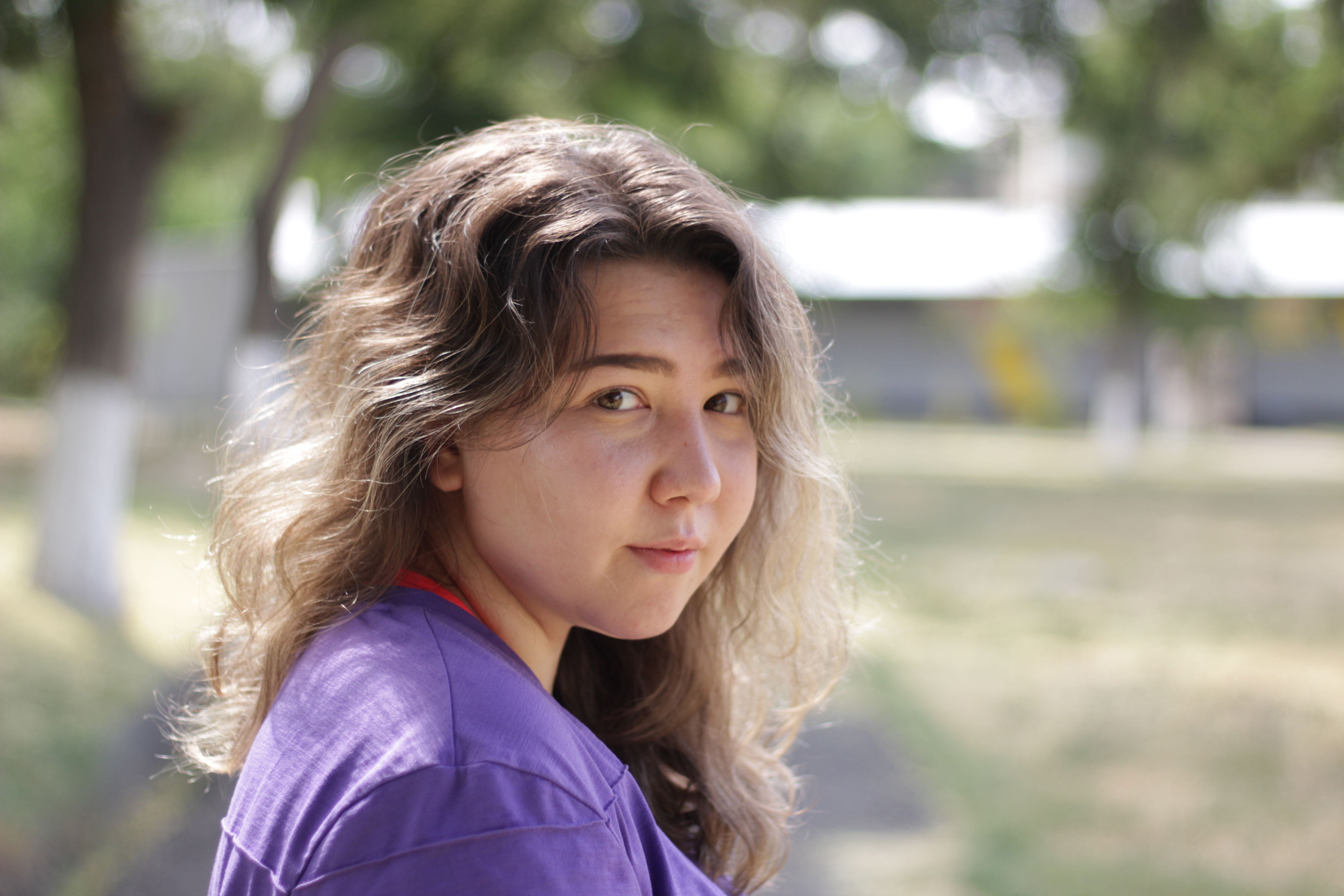 Close-up of a young woman with wavy hair, outdoors in natural light and shallow focus.