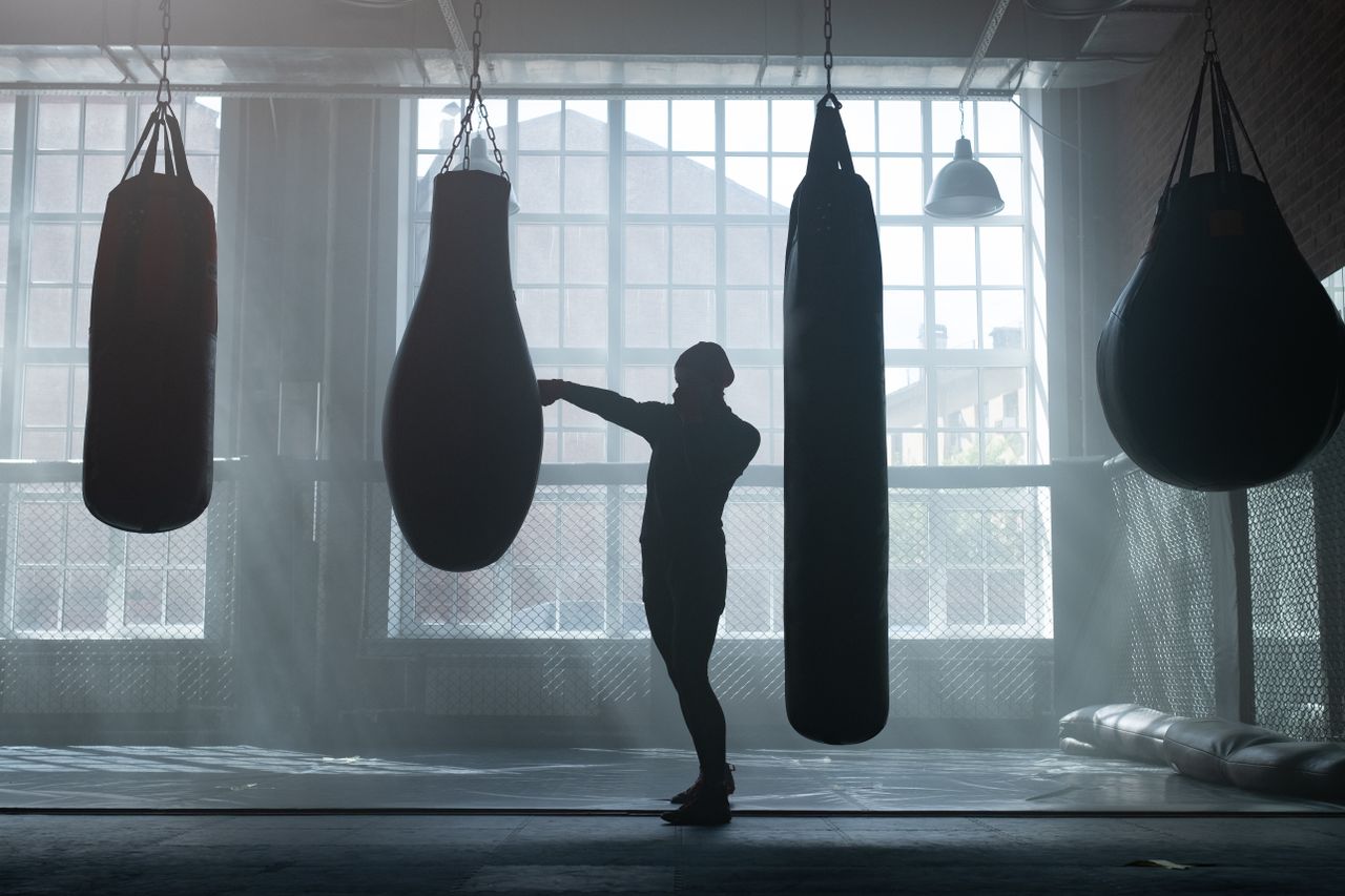 a silhouette of a person training with punching bags in an industrial