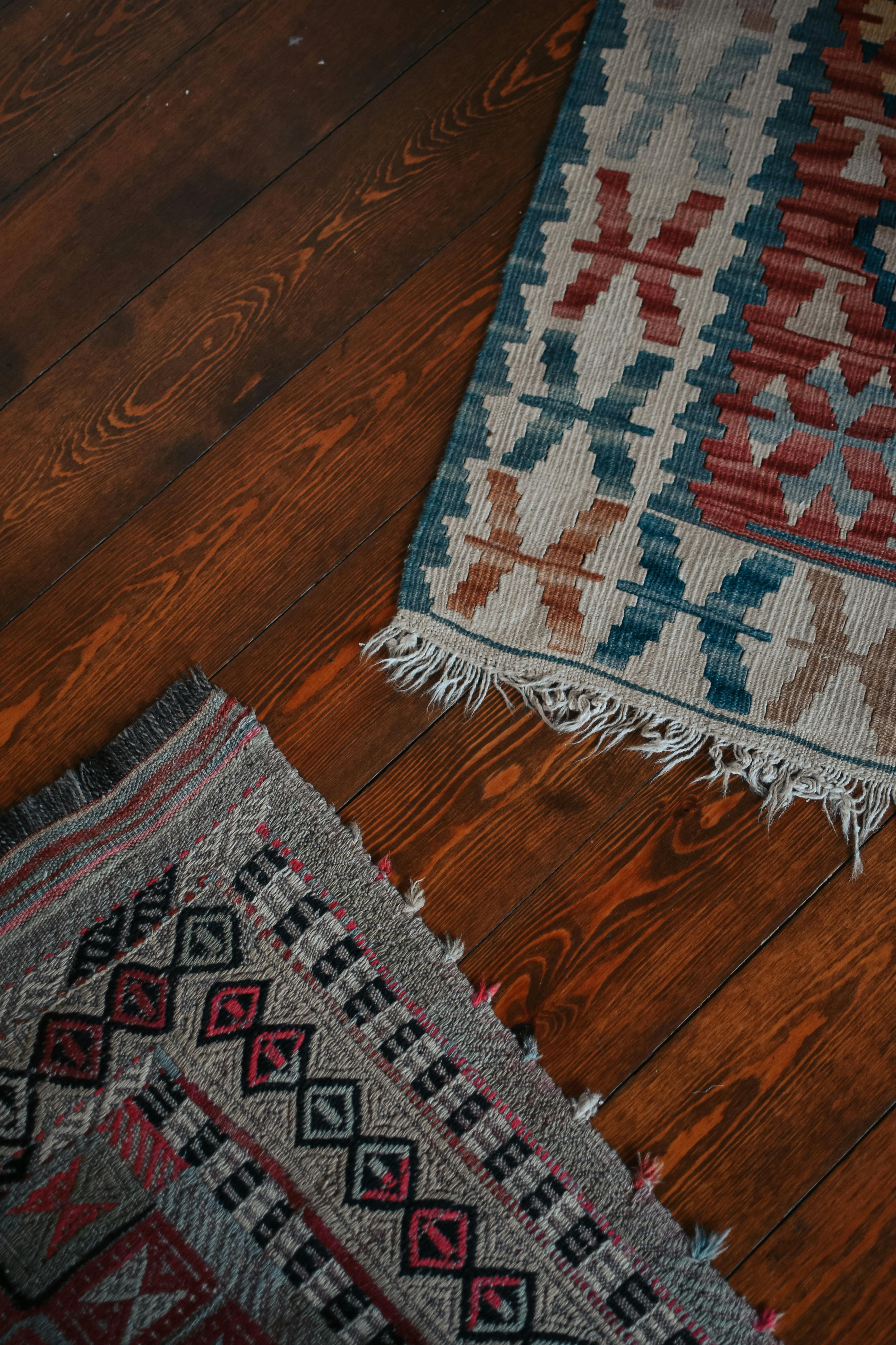 Intricate woven carpets placed on warm wooden floor, showcasing rich textures and patterns in a cozy setting.