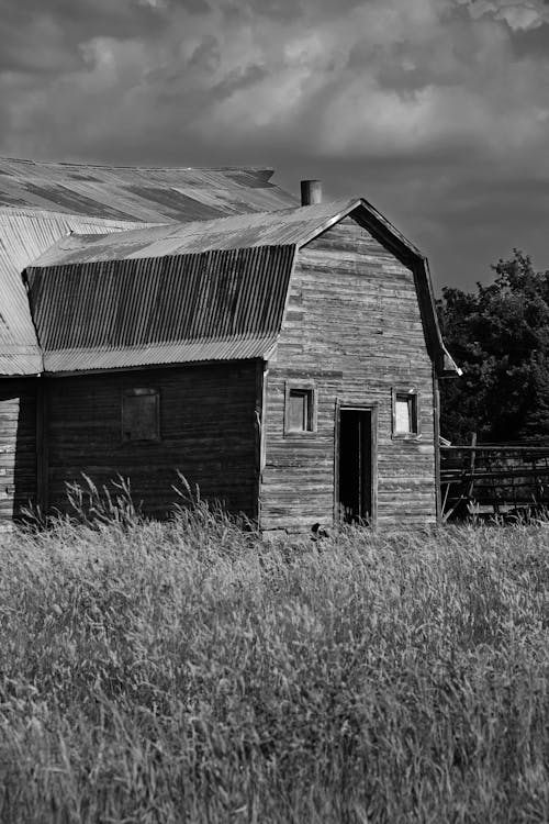 Grayscale Photo of a Barn Under a Cloudy Sky