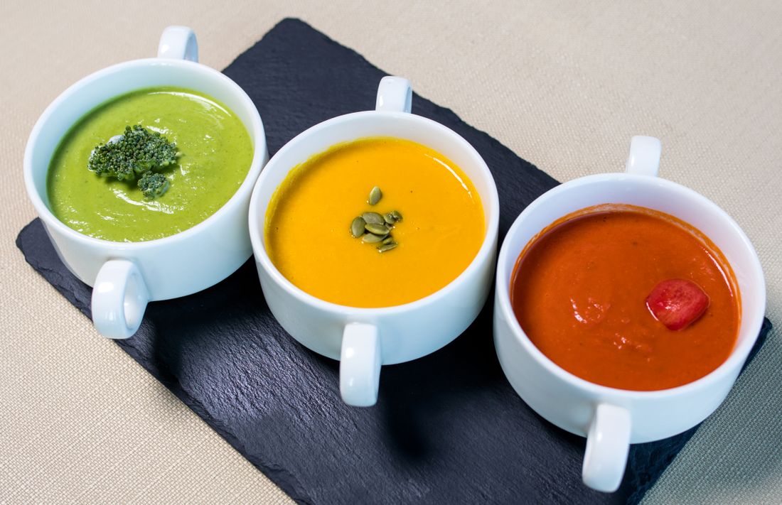 Three cups of green broccoli, golden pumpkin and red tomato cream soup on slate