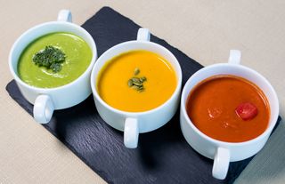Three cups of green broccoli, golden pumpkin and red tomato cream soup on slate