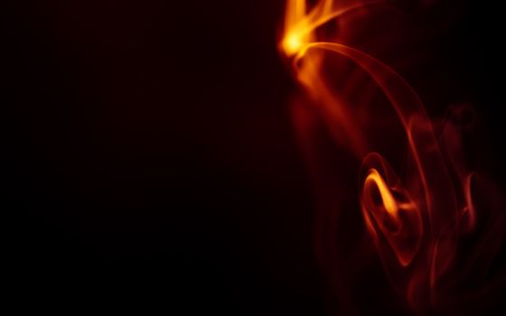 Close-up of swirling fire and smoke with dark background, creating a vibrant abstract scene.