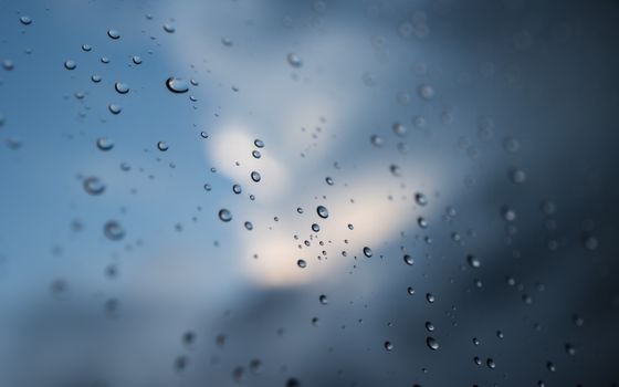 Close-up of raindrops on a window with a blurred sky backdrop, evoking a serene mood.