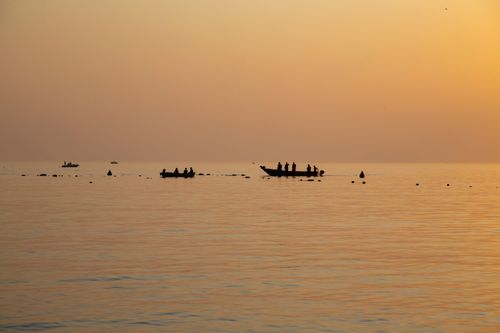 Free Fishermen on boats silhouetted against a serene sunset over the ocean. Stock Photo