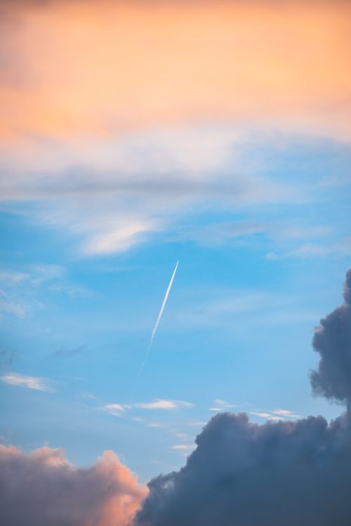Free A serene sky with a jet contrail against vibrant, colorful clouds at sunset. Stock Photo