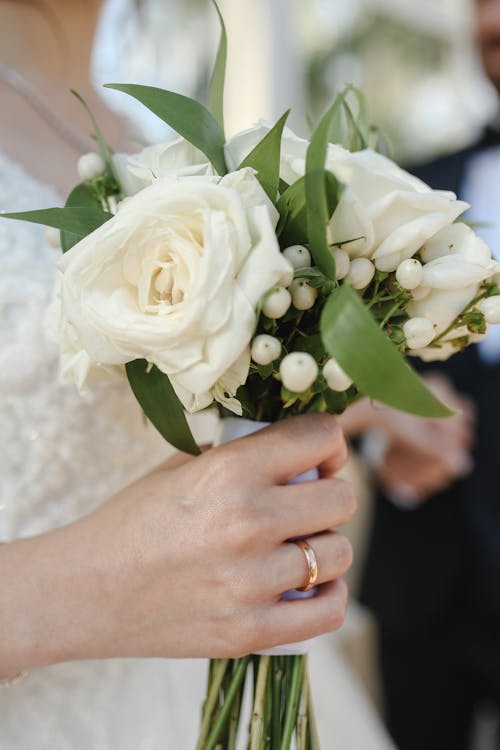 Woman Wearing Gold Wedding Ring Holding a White Bouquet of Flowers