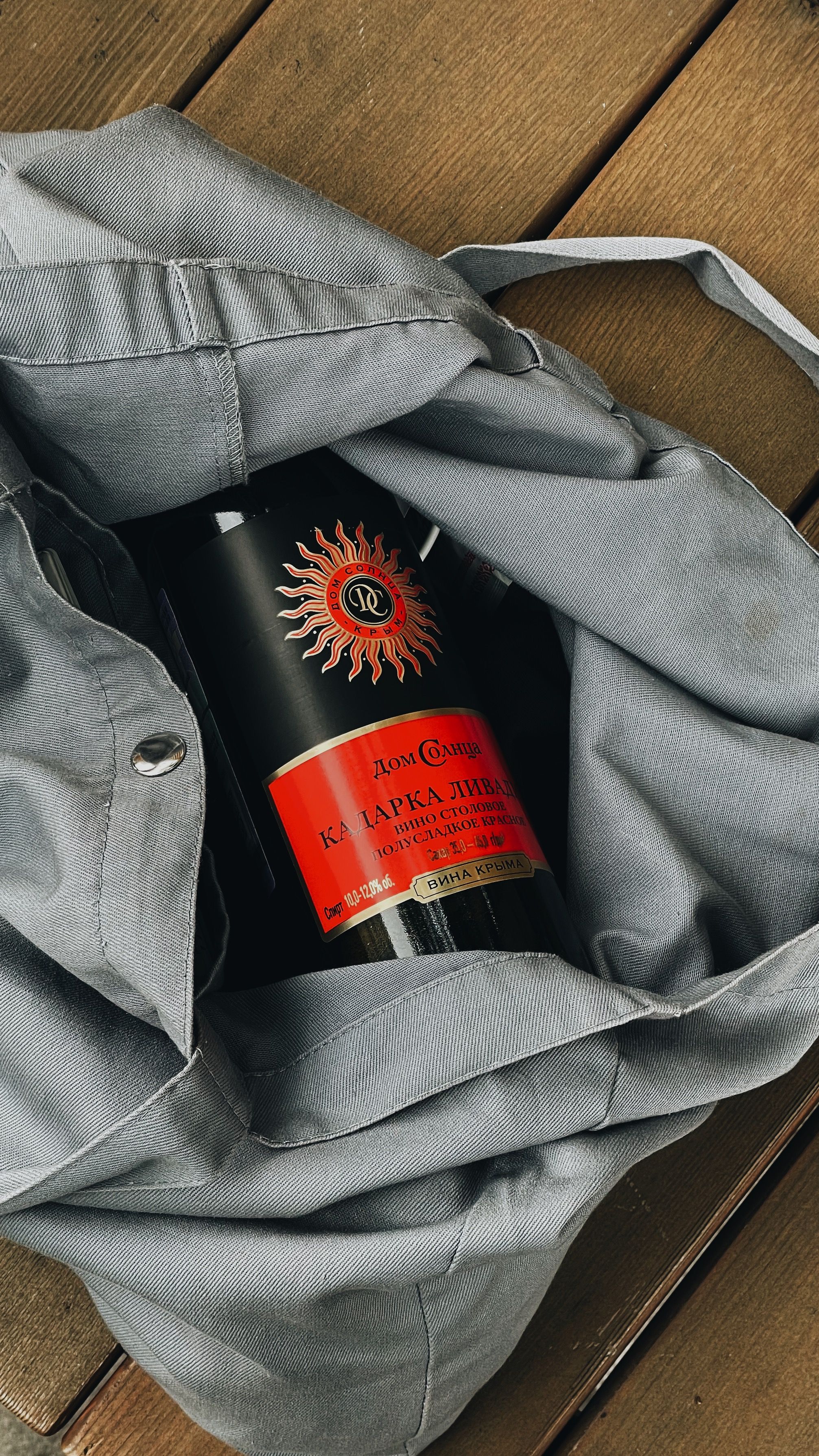 Close-up of a red labeled bottle inside a gray bag, placed on a wooden surface.