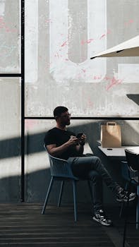 Man enjoying a coffee at an outdoor café, basking in sunlight and modern city vibes.