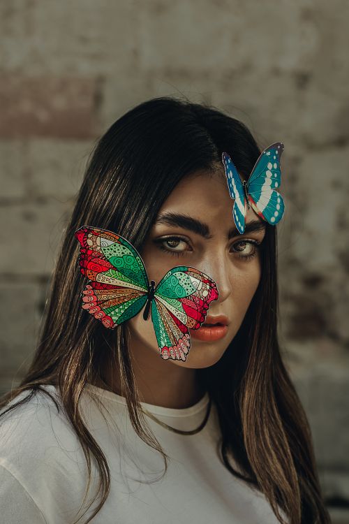 Free Artistic portrait of a woman adorned with vibrant butterflies, creating a unique visual statement. Stock Photo