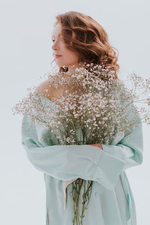 A Woman in Long Sleeves Holding a Bunch of Flowers while Looking Afar