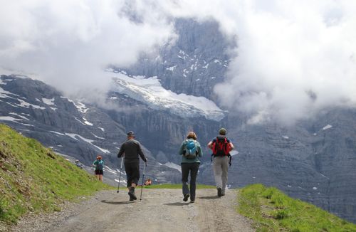 Free Group of hikers trekking on a mountain path with snow-capped peaks and cloudy skies. Stock Photo