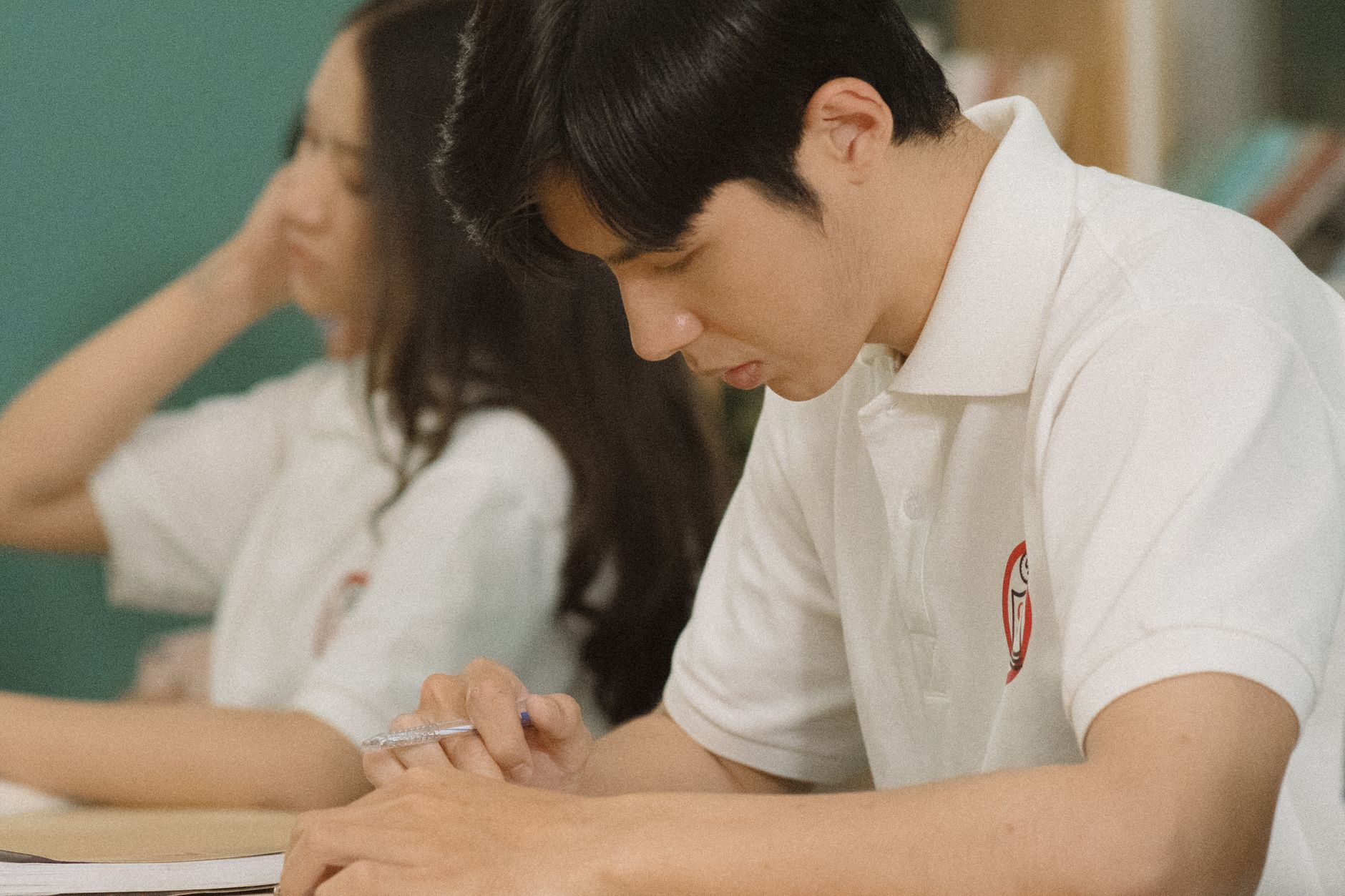 Students concentrating on studies indoors, one holding a pen and writing notes.