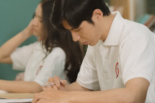 Students concentrating on studies indoors, one holding a pen and writing notes.
