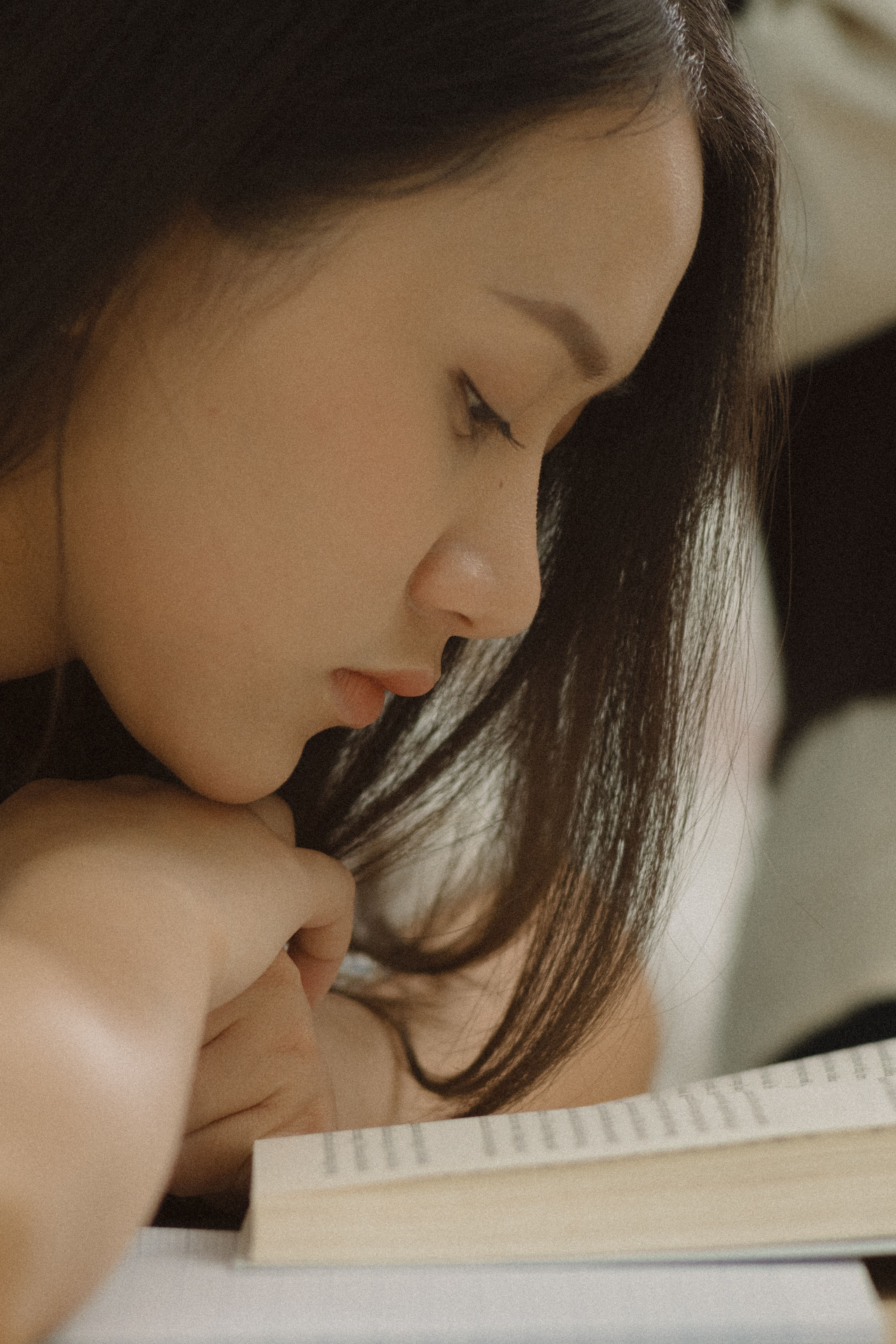 Side view of an Asian woman intently reading a book, highlighting focus and learning.