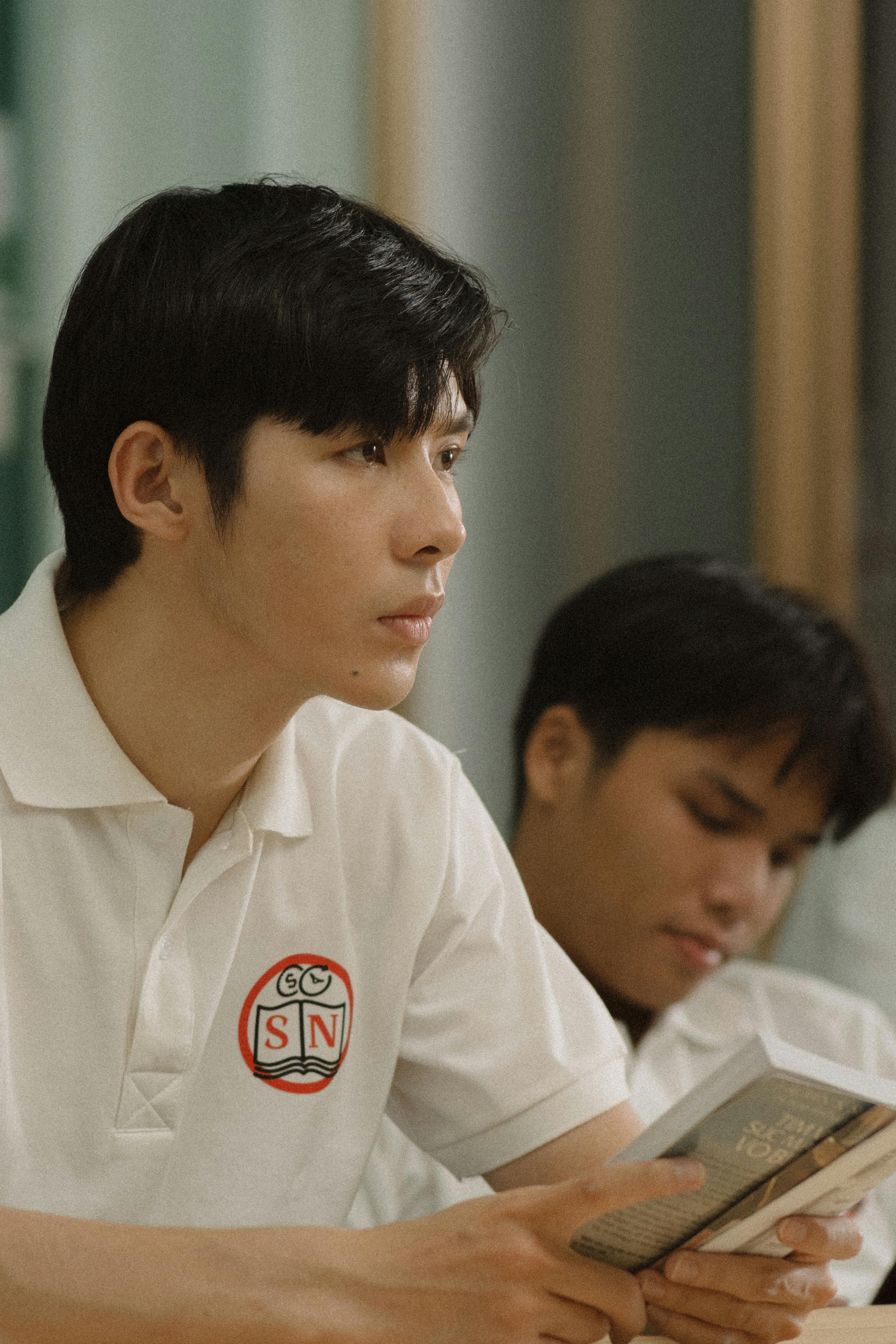 Portrait of an introspective young man in a polo shirt holding a book indoors.