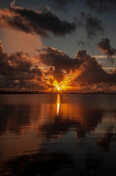 A stunning sunset over an ocean horizon with dramatic clouds reflecting on calm water.