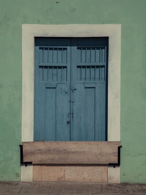 Free A vibrant blue wooden door on an aged green wall with attached bench, perfect for urban exploration. Stock Photo
