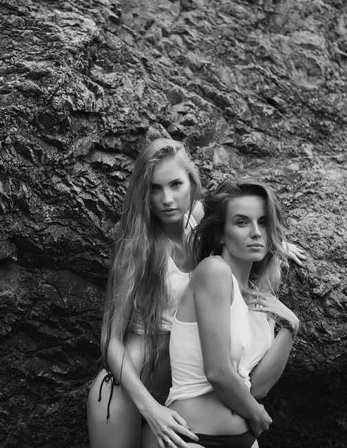 A captivating monochrome portrait of two women posing against a rugged rock face, showcasing natural beauty and elegance.