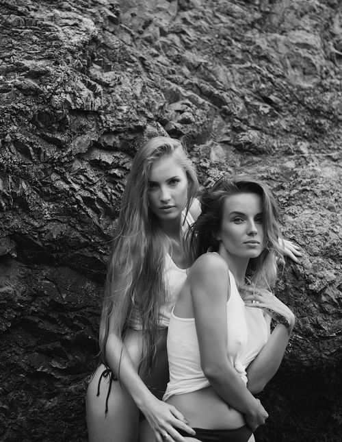 Free A captivating monochrome portrait of two women posing against a rugged rock face, showcasing natural beauty and elegance. Stock Photo