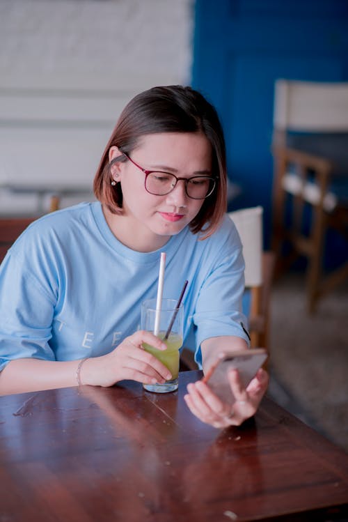 Woman Holding a Glass While Using Cellphone