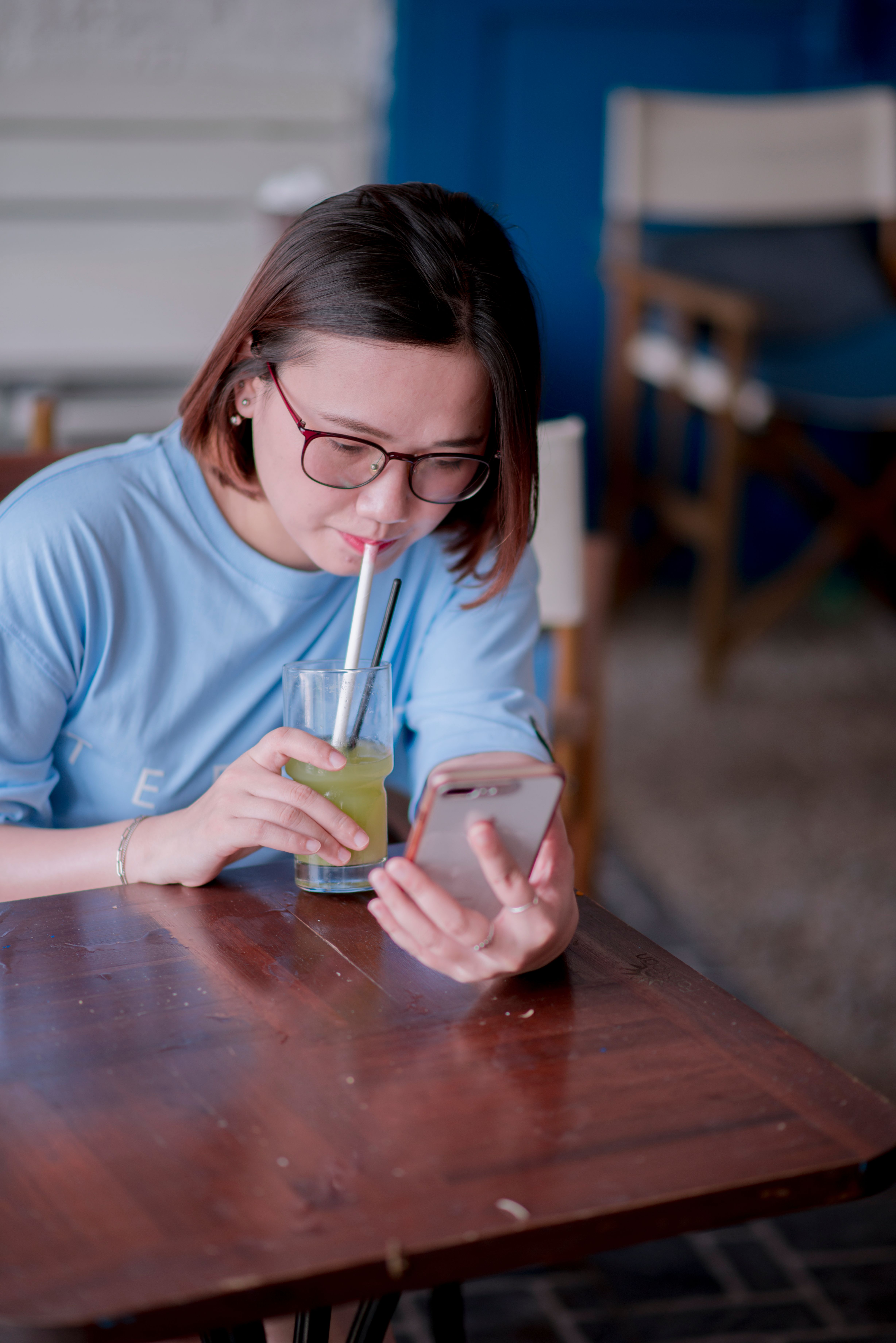 Woman Drinking a Green Beverage while Using Her Cell Phone