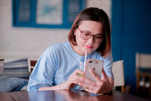 Close-Up Shot of a Woman Holding a Glass of Beverage while Using a Mobile Phone