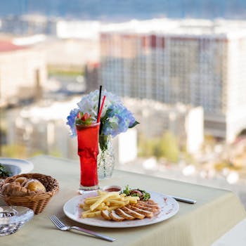 Plate of fries and chicken with cocktail on restaurant table overlooking cityscape.