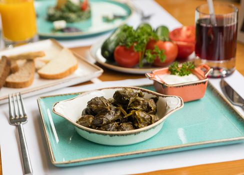 Close-up of Mediterranean dolma dish with fresh vegetables and drinks on dining table.