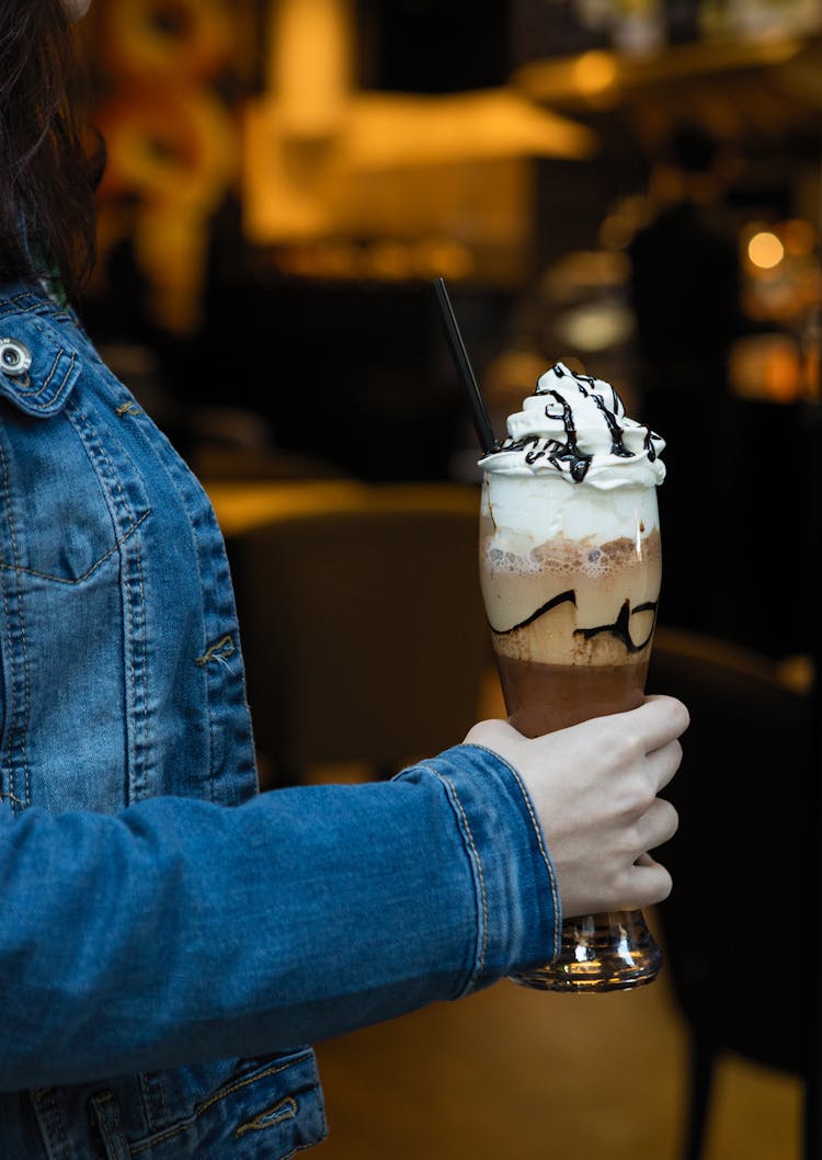 A Person Wearing Denim Jacket Holding A Glass Of Chocolate Milkshake With 