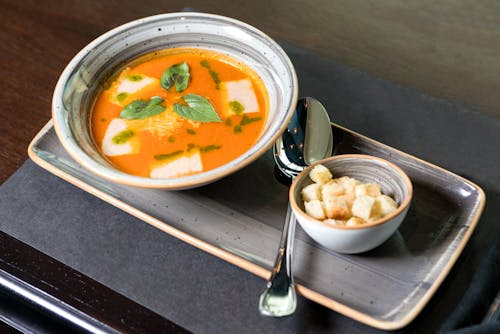 A Yellow Soup Decorated with Leaves in a Bowl Beside a Bowl of Croutons