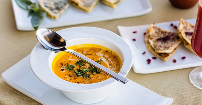 A bowl of creamy pumpkin soup garnished with herbs, paired with flatbread and sauce.