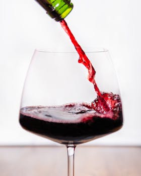 A vibrant close-up shot capturing red wine pouring into a glass with a white background.