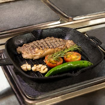 Juicy grilled steak accompanied by tomatoes, garlic, pepper, and rosemary in a cast iron pan.