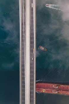 Aerial shot of a bridge spanning a waterway with ships below, showcasing transportation dynamics.