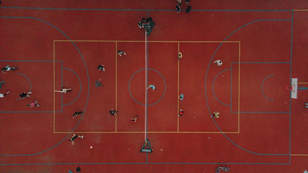 Dynamic aerial perspective of people playing on a vibrant red basketball court in a lively setting.