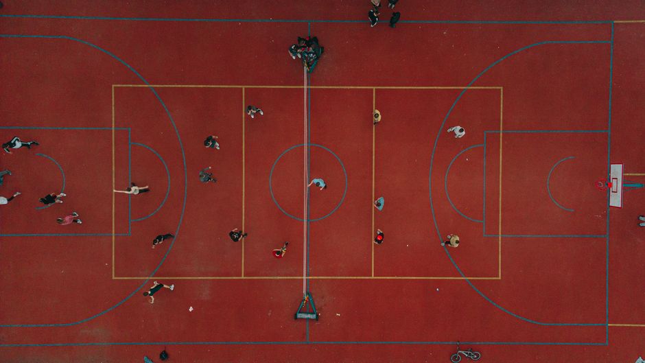 Dynamic aerial perspective of people playing on a vibrant red basketball court in a lively setting.