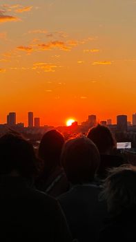 Silhouetted people watching a vibrant sunset over Moscow's skyline, creating a serene atmosphere.