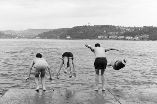 Grayscale Photo of Men Jumping on Beach