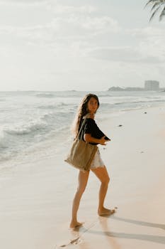 Caucasian woman walking on a beach in Sri Lanka, carrying a bag, with waves and palm trees in the background.